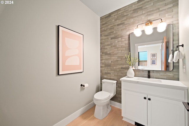 bathroom featuring brick wall, hardwood / wood-style flooring, vanity, and toilet