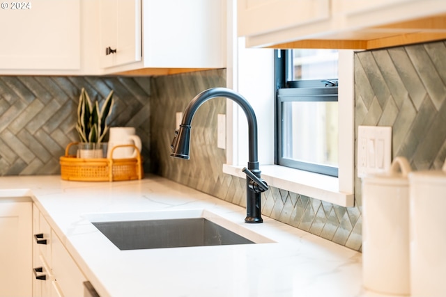 interior details with sink, tasteful backsplash, white cabinetry, and light stone countertops