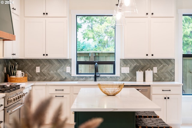 kitchen with stainless steel appliances, sink, white cabinets, wall chimney exhaust hood, and pendant lighting