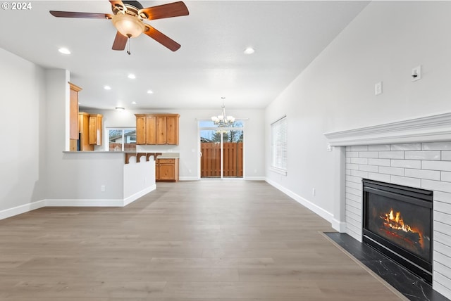 unfurnished living room featuring ceiling fan with notable chandelier, wood-type flooring, and a brick fireplace