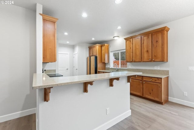 kitchen with sink, light hardwood / wood-style flooring, kitchen peninsula, fridge, and a breakfast bar