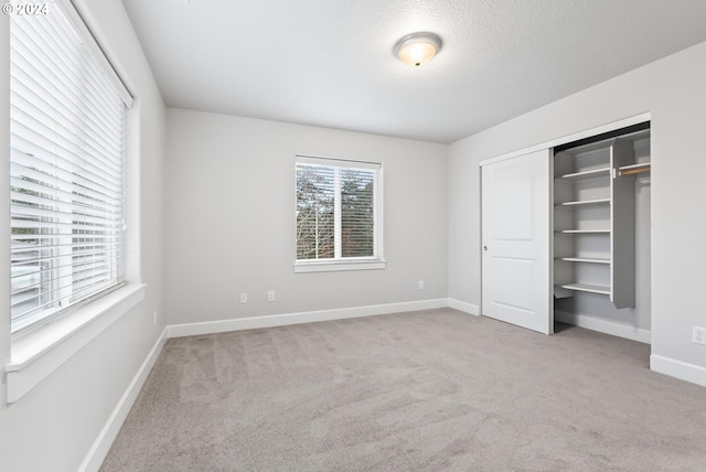 unfurnished bedroom featuring light carpet, a closet, and a textured ceiling