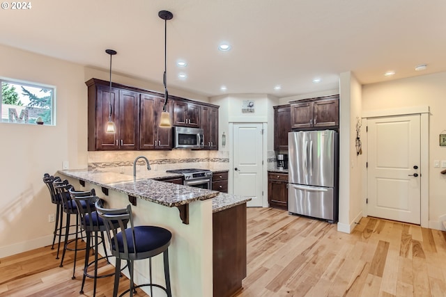 kitchen featuring appliances with stainless steel finishes, light stone counters, tasteful backsplash, light wood-type flooring, and decorative light fixtures