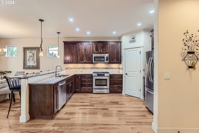 kitchen with hanging light fixtures, sink, kitchen peninsula, appliances with stainless steel finishes, and a kitchen breakfast bar