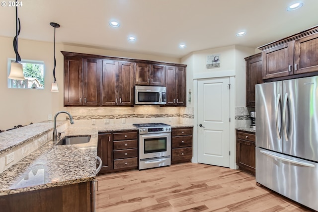 kitchen with appliances with stainless steel finishes, light wood-type flooring, sink, and decorative light fixtures