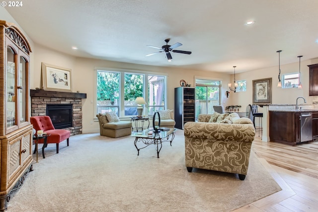 living room with ceiling fan, a stone fireplace, light wood-type flooring, and sink