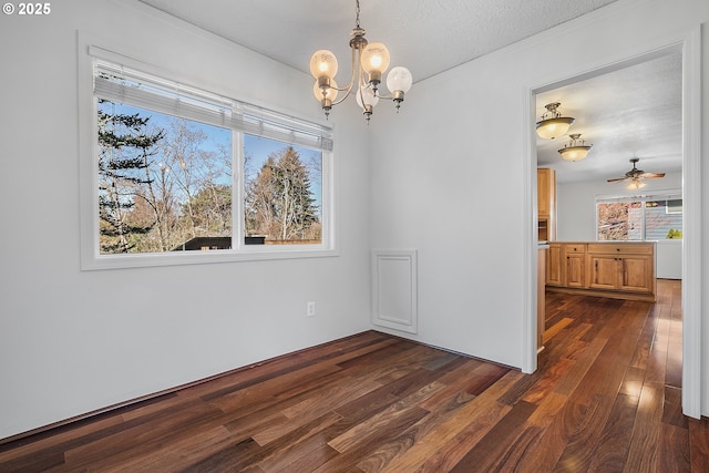 unfurnished dining area featuring dark wood finished floors, ceiling fan with notable chandelier, a healthy amount of sunlight, and a textured ceiling