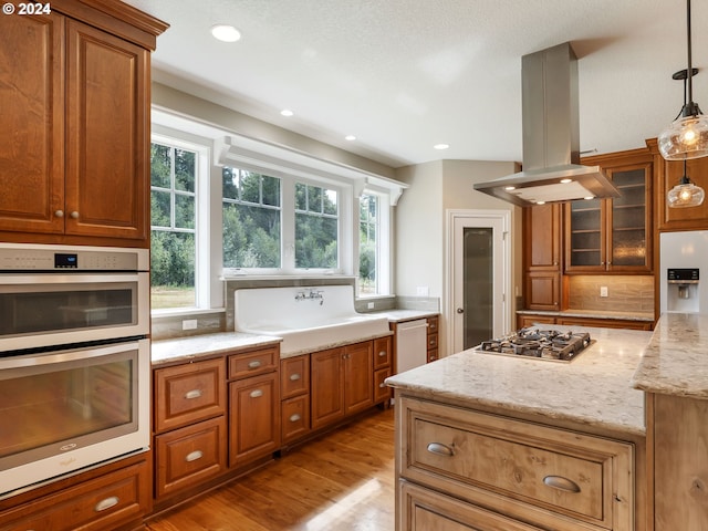 kitchen featuring light wood-type flooring, light stone countertops, stainless steel appliances, pendant lighting, and island range hood