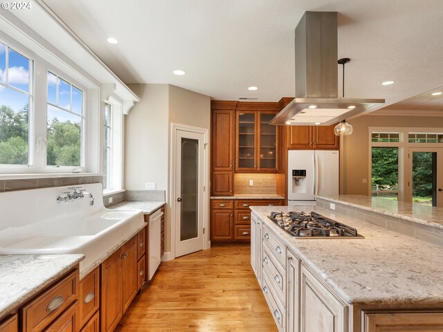 kitchen featuring light wood-type flooring, decorative backsplash, pendant lighting, island range hood, and white appliances