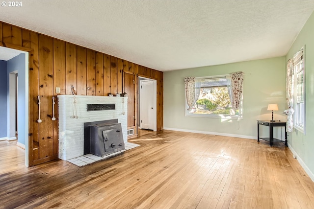 unfurnished living room with wood walls, a wood stove, light hardwood / wood-style flooring, and a textured ceiling