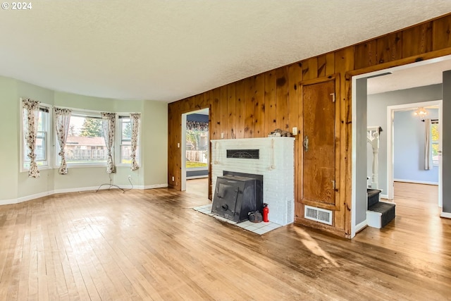 unfurnished living room featuring hardwood / wood-style flooring, a wood stove, a textured ceiling, and wooden walls