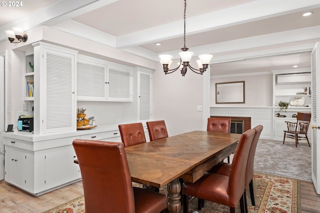 dining area featuring crown molding, a chandelier, a brick fireplace, beamed ceiling, and light hardwood / wood-style floors