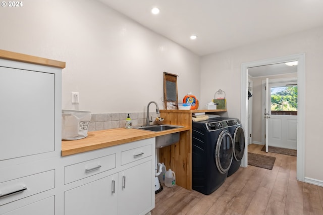 clothes washing area with cabinets, sink, independent washer and dryer, and light hardwood / wood-style flooring