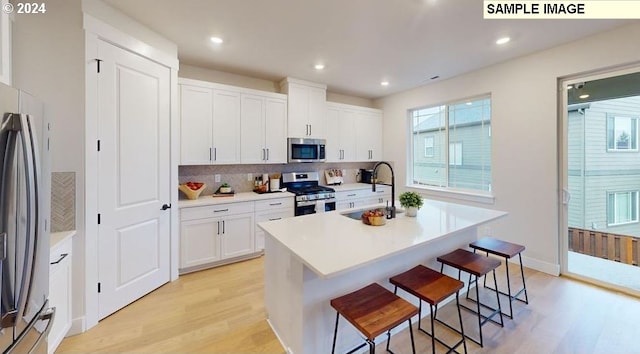 kitchen featuring appliances with stainless steel finishes, sink, white cabinets, a center island with sink, and light wood-type flooring