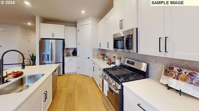 kitchen with sink, white cabinetry, light wood-type flooring, appliances with stainless steel finishes, and decorative backsplash