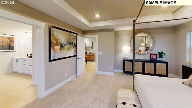 bedroom featuring light carpet, ensuite bath, and a raised ceiling