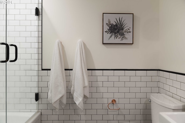 bathroom with tile walls, toilet, and a shower with door