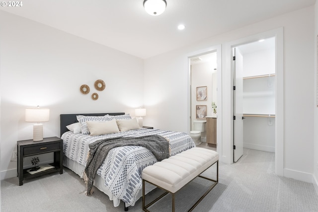 bedroom featuring a spacious closet, connected bathroom, light colored carpet, and a closet