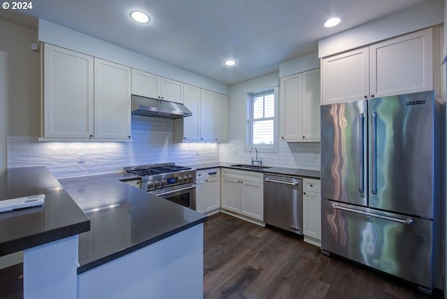 kitchen featuring dark countertops, under cabinet range hood, high quality appliances, white cabinets, and a sink