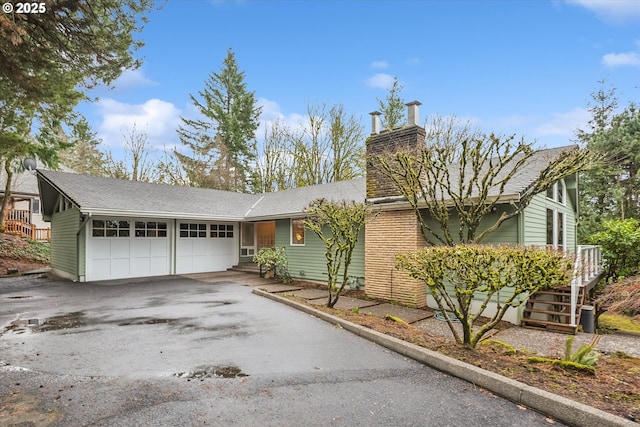 ranch-style house with a garage, a chimney, and aphalt driveway