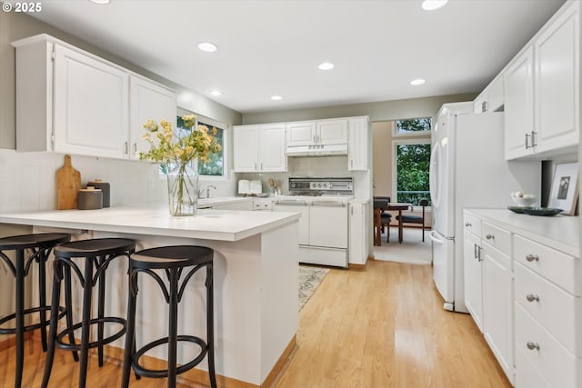 kitchen with a peninsula, under cabinet range hood, electric range, and plenty of natural light