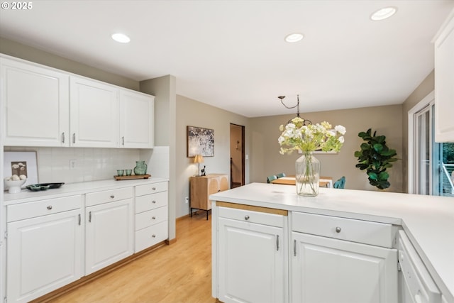 kitchen with pendant lighting, light countertops, light wood-style flooring, backsplash, and white cabinets