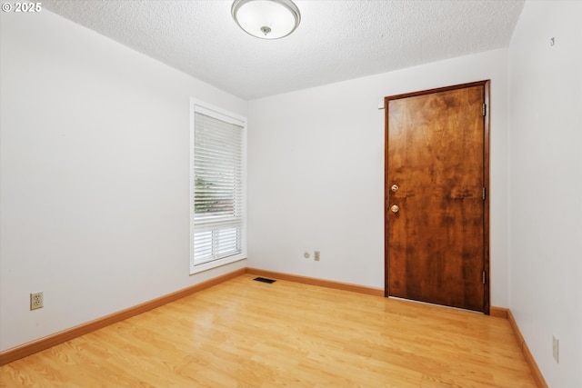 empty room featuring a textured ceiling, light wood-style flooring, visible vents, and baseboards