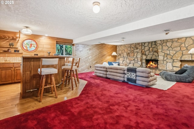 living area featuring a fireplace, light colored carpet, wood walls, a textured ceiling, and a bar