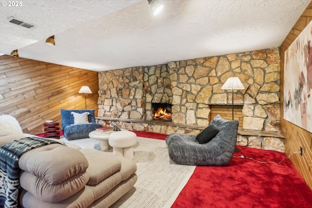 living area featuring a textured ceiling, wood walls, a fireplace, and visible vents