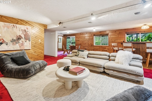 carpeted living room featuring visible vents, wooden walls, and a textured ceiling