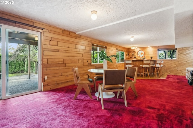 carpeted dining space with a textured ceiling, wooden walls, and a wealth of natural light