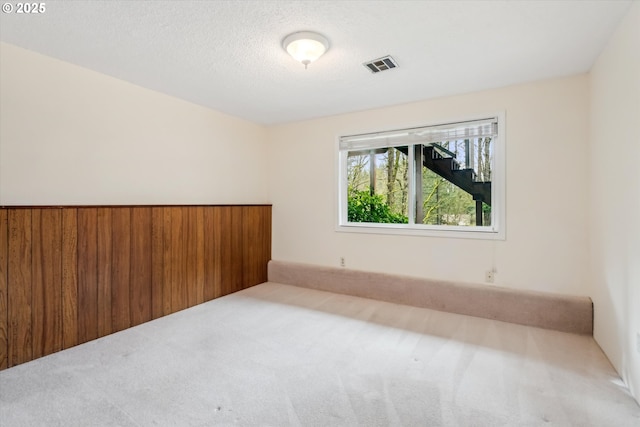 empty room with carpet floors, visible vents, and a textured ceiling