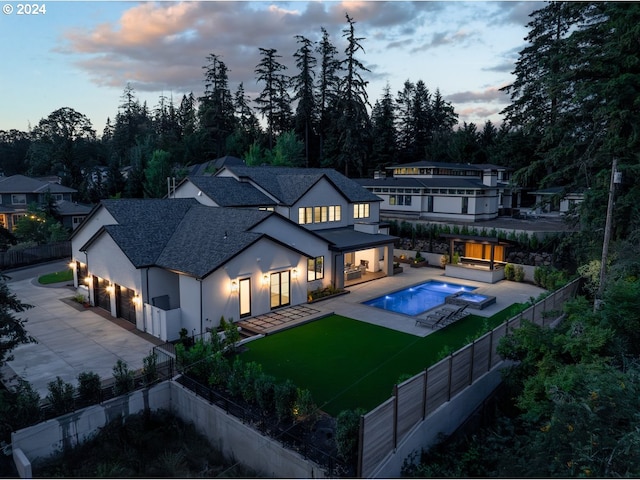 back house at dusk with a yard, a patio area, and a pool with hot tub