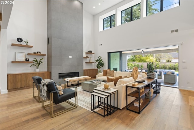 living room with a towering ceiling, a tile fireplace, light hardwood / wood-style floors, and ceiling fan