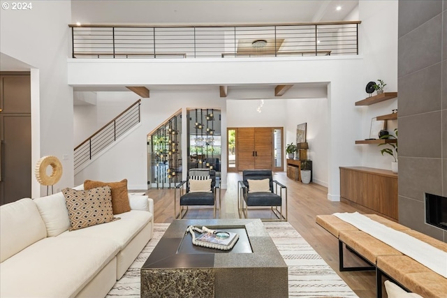 living room featuring a tile fireplace, a towering ceiling, and light hardwood / wood-style flooring