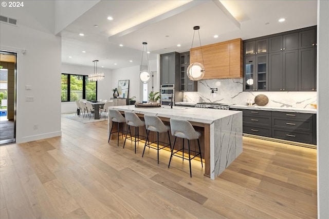 kitchen with light stone countertops, pendant lighting, backsplash, and a spacious island