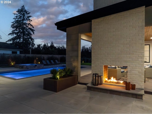 pool at dusk with a patio, an outdoor fireplace, and an in ground hot tub