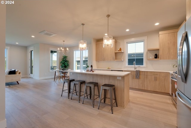 kitchen with light brown cabinetry, a center island with sink, light wood-type flooring, and a healthy amount of sunlight