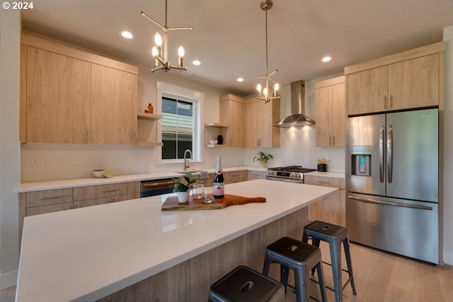 kitchen featuring light hardwood / wood-style floors, wall chimney exhaust hood, a kitchen breakfast bar, appliances with stainless steel finishes, and light brown cabinetry