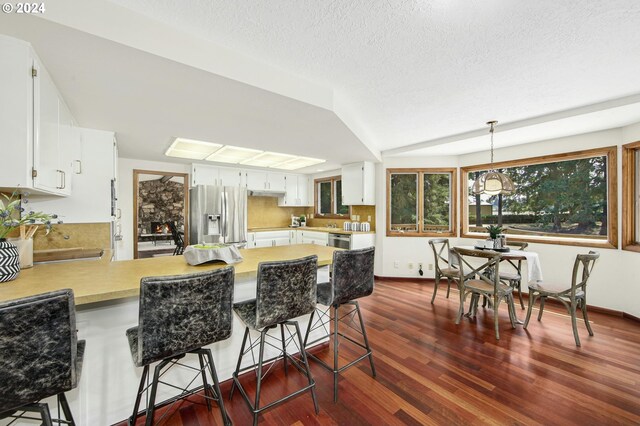 kitchen featuring kitchen peninsula, hanging light fixtures, appliances with stainless steel finishes, and dark wood-type flooring