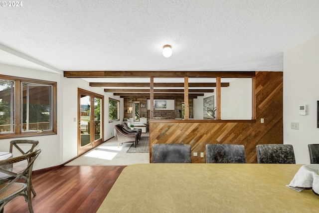 living room featuring a textured ceiling, beam ceiling, wooden walls, and light hardwood / wood-style flooring