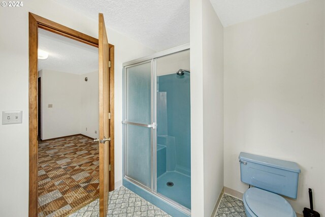 bathroom featuring a textured ceiling, toilet, a shower with door, and tile patterned floors