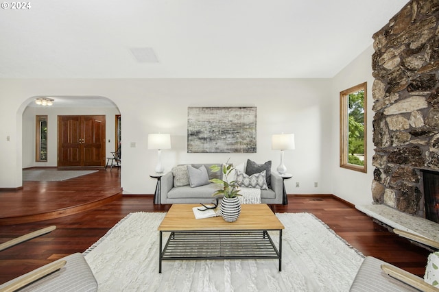 living room with a stone fireplace, dark wood-type flooring, and lofted ceiling