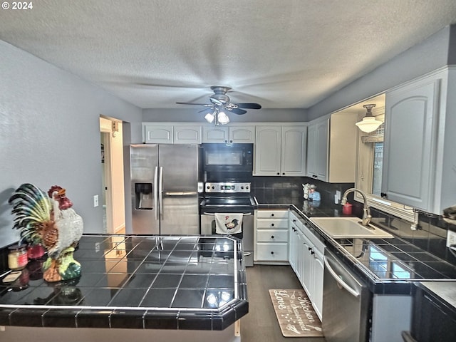 kitchen with sink, dark wood-type flooring, appliances with stainless steel finishes, tile counters, and a textured ceiling