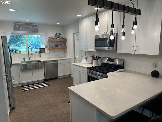 kitchen with dark wood-type flooring, stainless steel appliances, kitchen peninsula, pendant lighting, and white cabinets