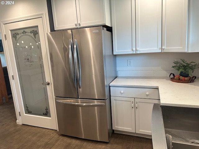 kitchen with stainless steel fridge, light stone counters, dark hardwood / wood-style flooring, and white cabinets