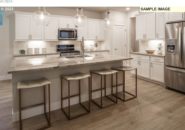 kitchen with backsplash, a center island with sink, hanging light fixtures, and appliances with stainless steel finishes