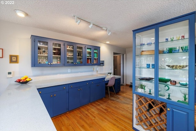 bar with blue cabinetry, light wood-type flooring, a textured ceiling, and track lighting