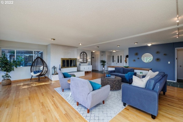 living room with wood-type flooring, a textured ceiling, and a brick fireplace