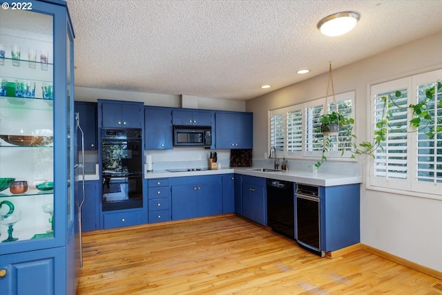 kitchen featuring blue cabinetry, sink, a textured ceiling, black appliances, and light wood-type flooring